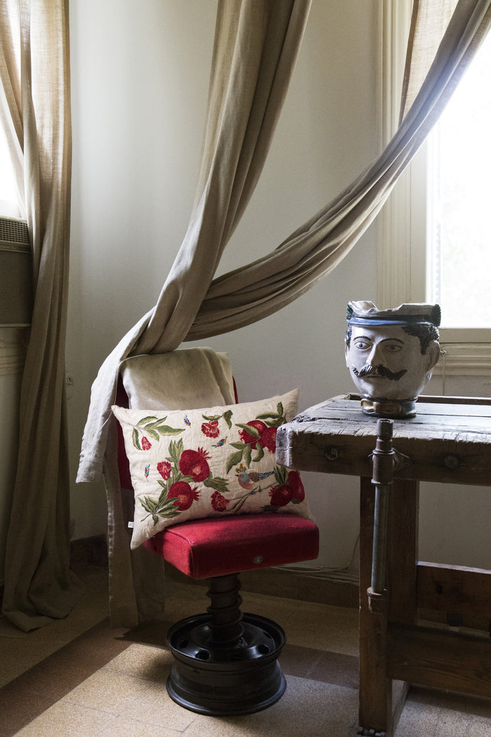 Pomegranate embroidered cushion on a red velvet stool beside a carved bust