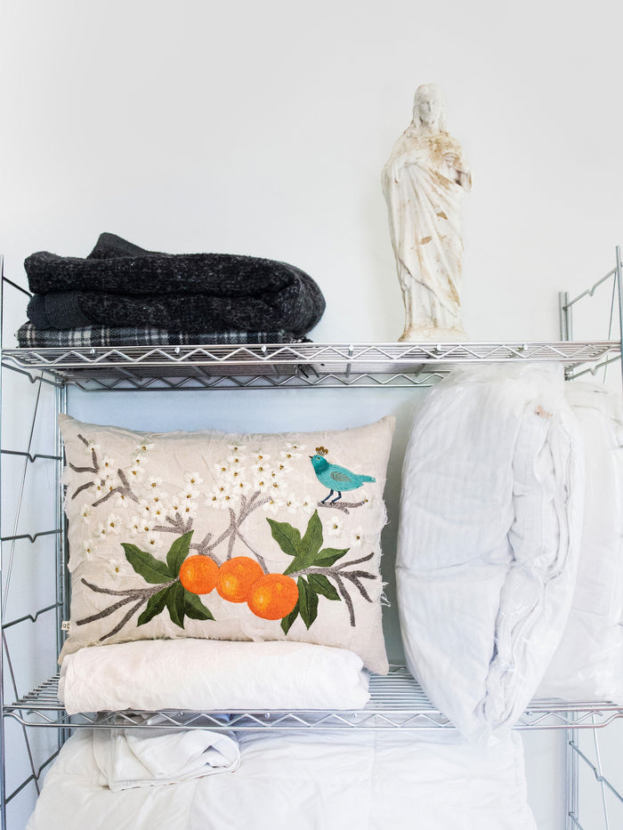 Orange Blossom embroidered cushion among folded throws on a metal shelf