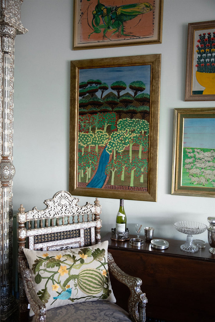 Watermelon embroidered cushion on an armchair under a wall of paintings