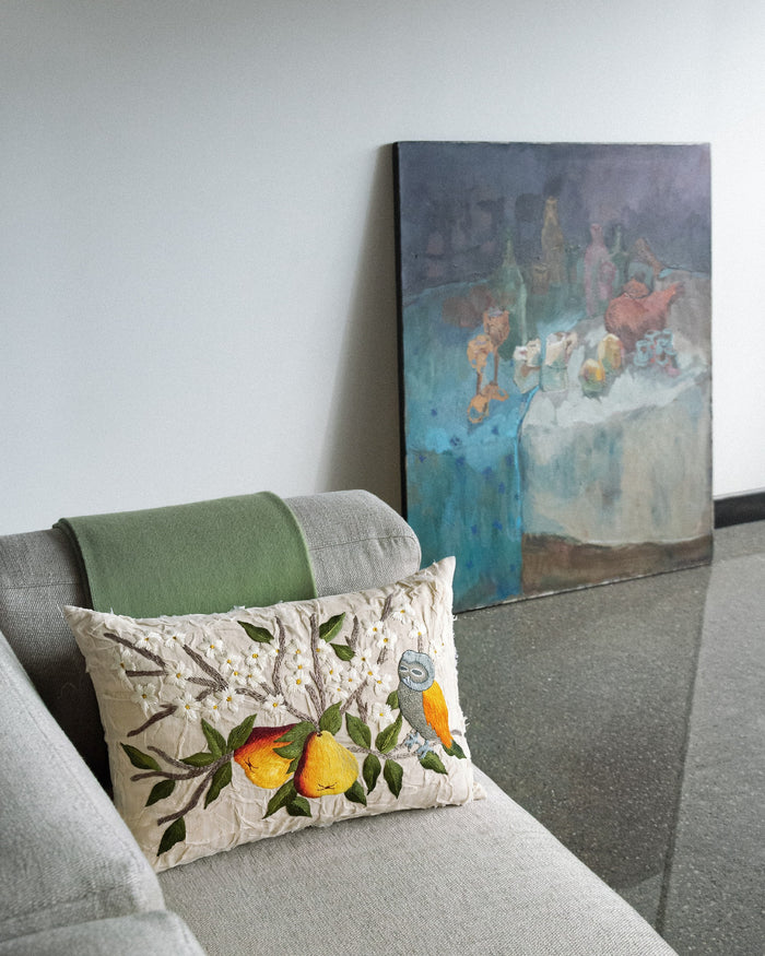Pears and Owl embroidered cushion on a grey sofa in front of a painting